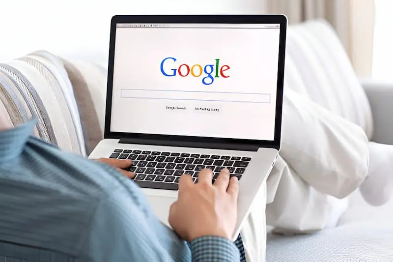 Person using a laptop displaying the Google homepage while seated on a couch.